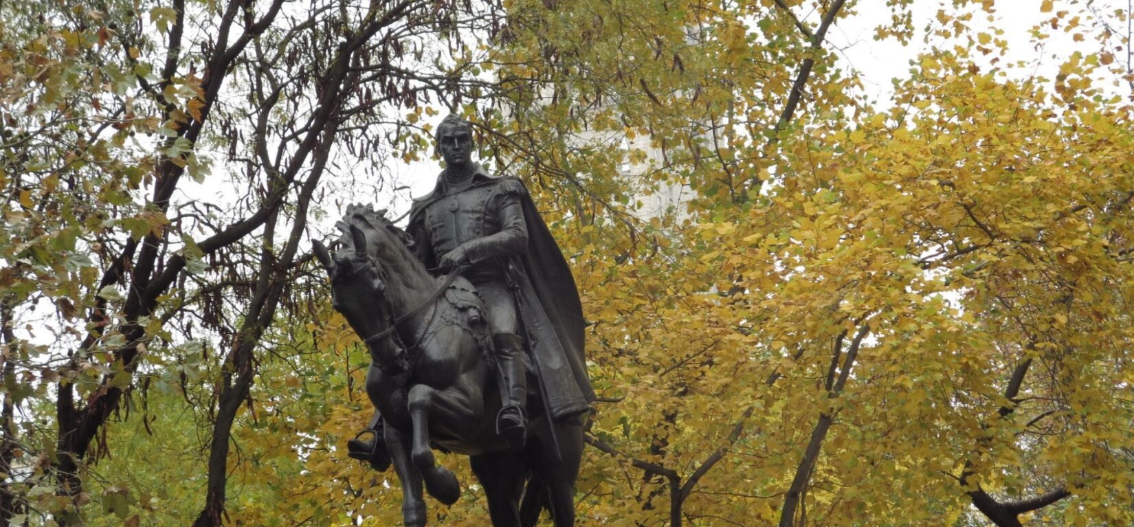 The statue is seen against a backdrop of trees fresh with leaves of spring.