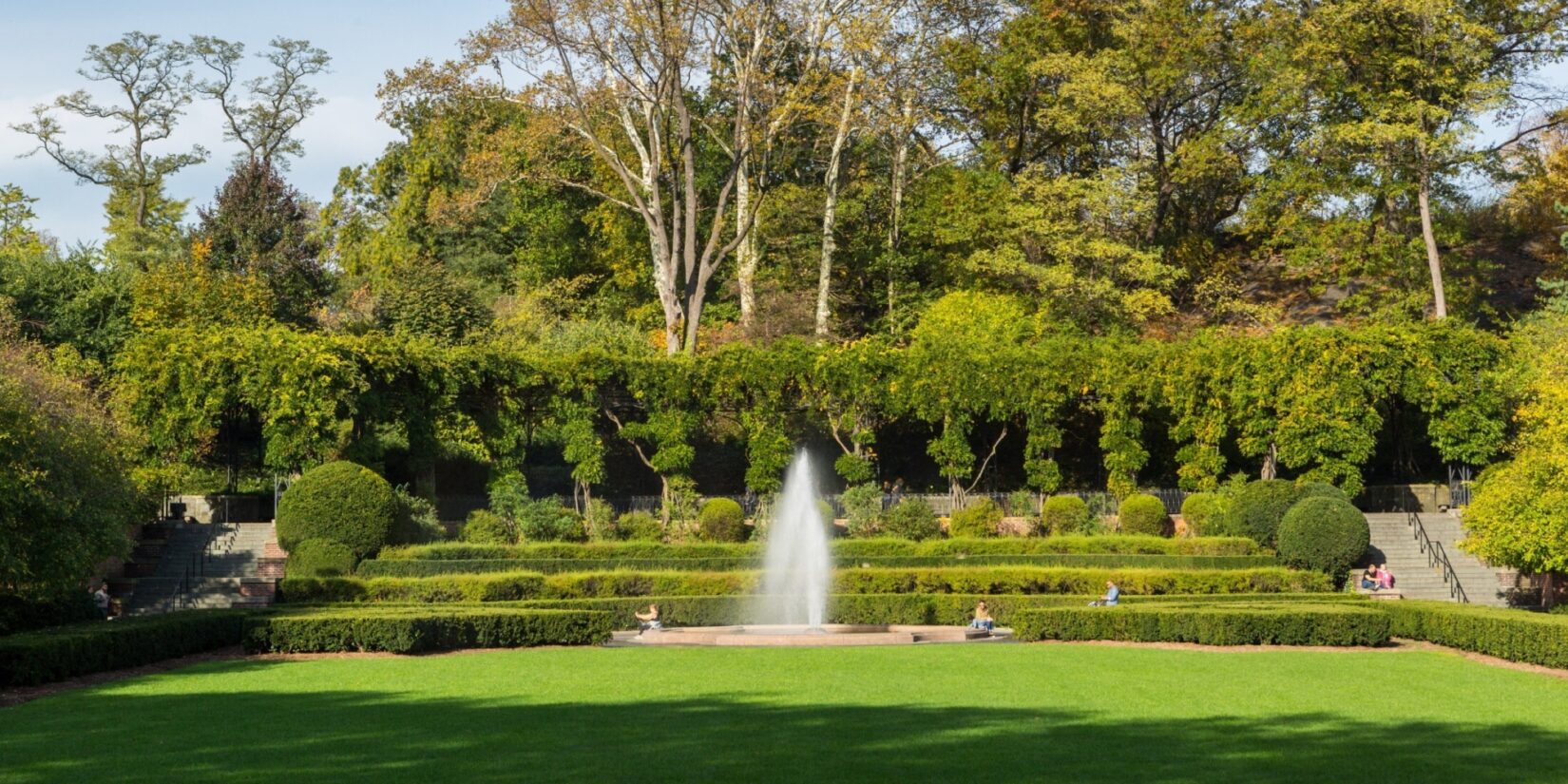 The fountain is pictured with the wisteria pergola behind it on a clear Spring day.