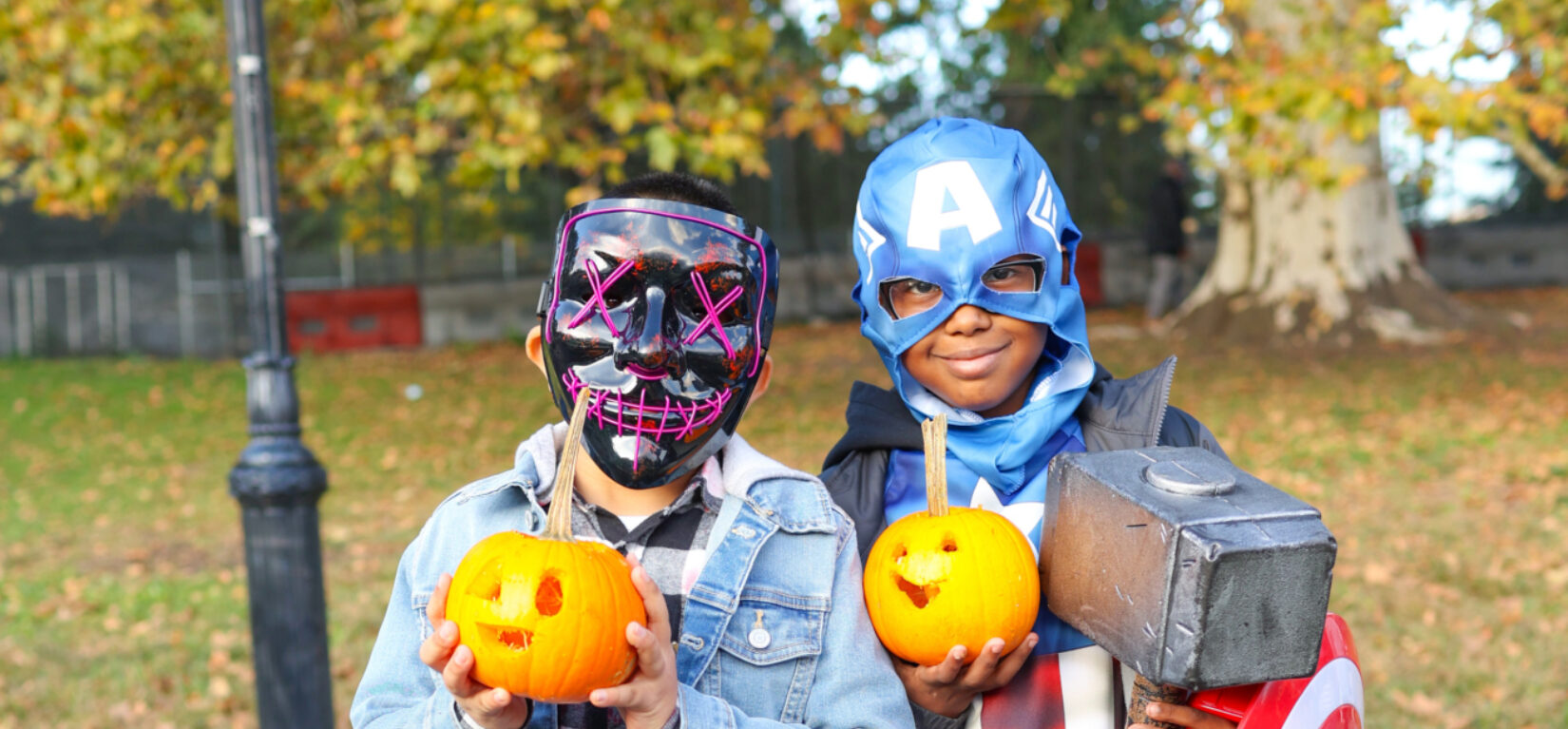 Two kids in Halloween dress hold up pumpkins in Central Park