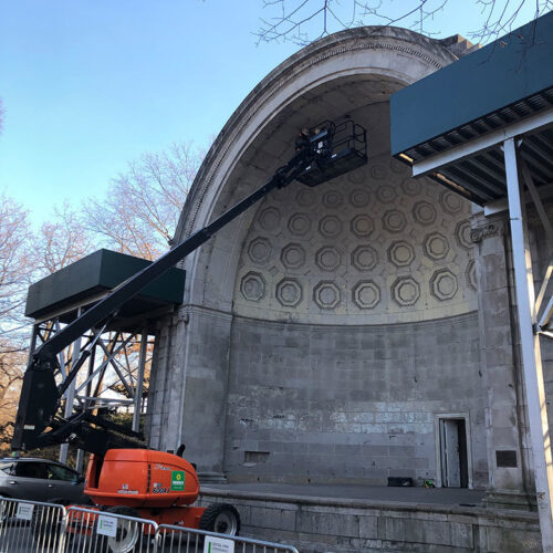 A crane lifts inspectors to the underside of the top of the bandshell