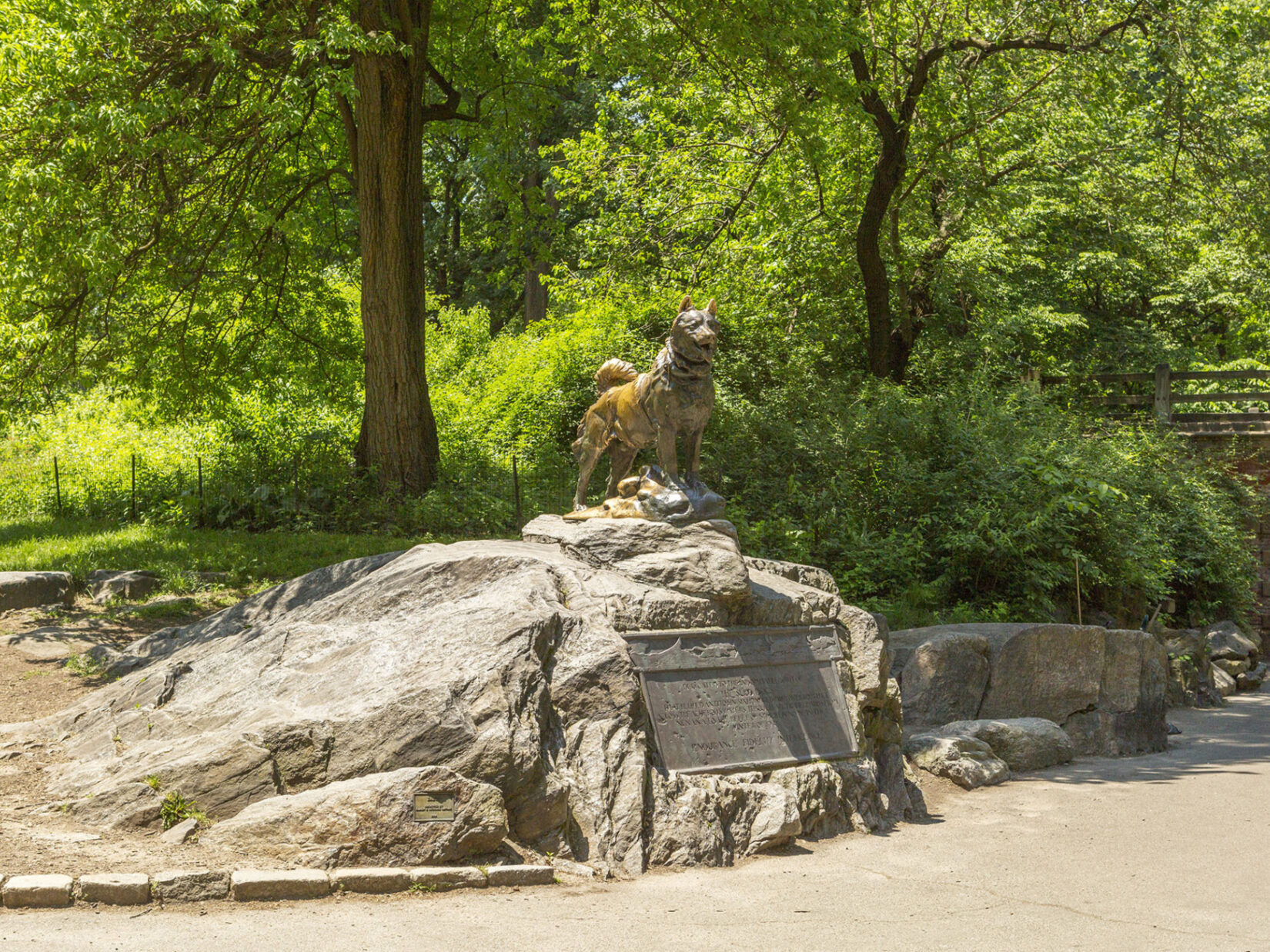 Balto is seen standing proudly on his rock, above the accompanying plaque, on a sunny day