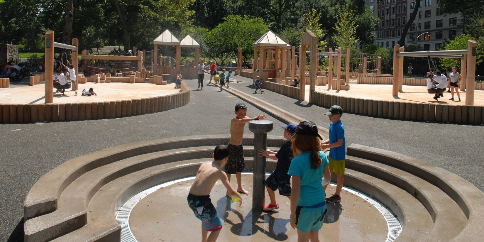 Several children surround the water feature on a cloudless summer day