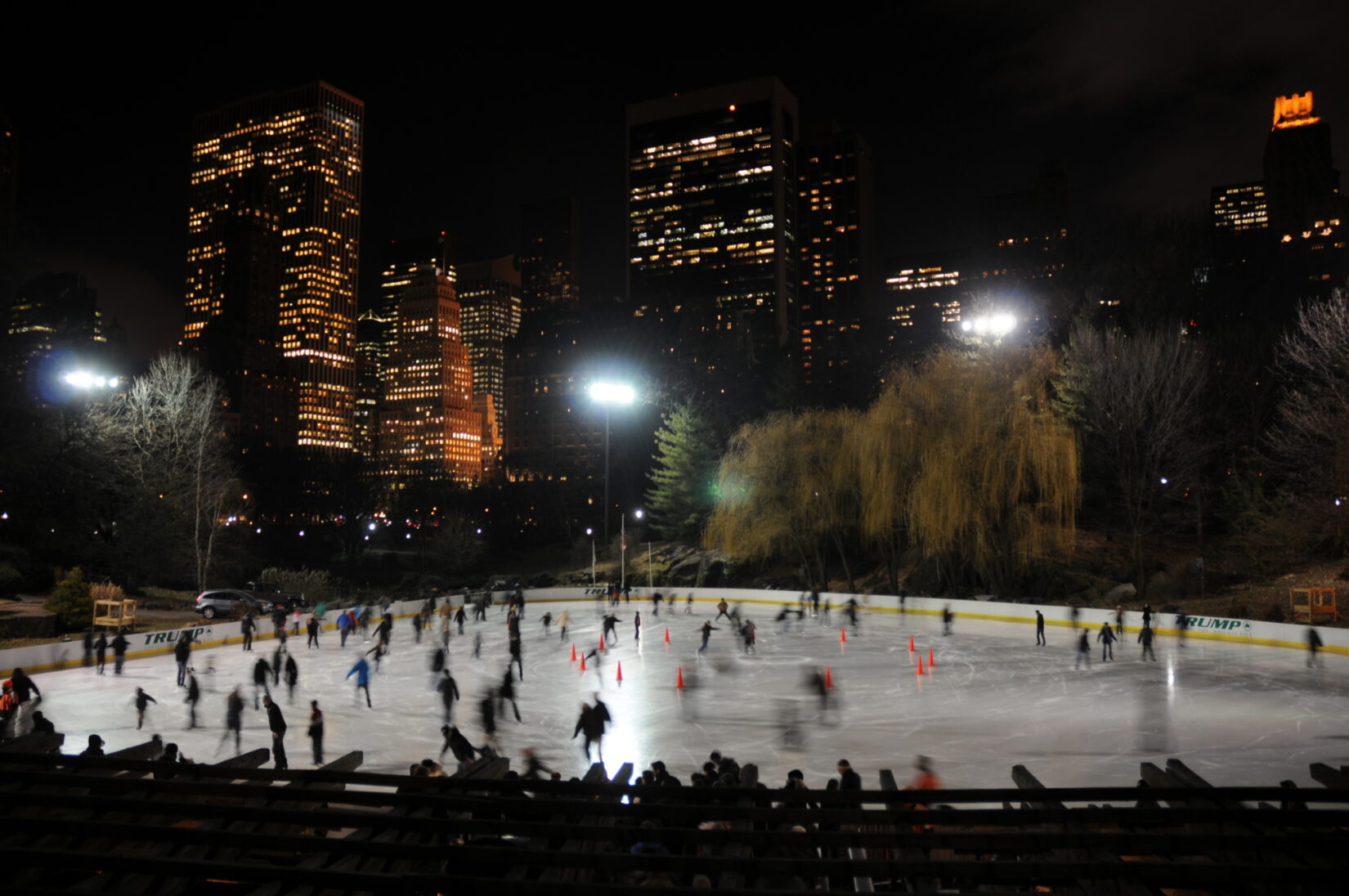 Skaters enjoy the Wollman Rink after dark, with the skyline of Manhattan as a backdrop