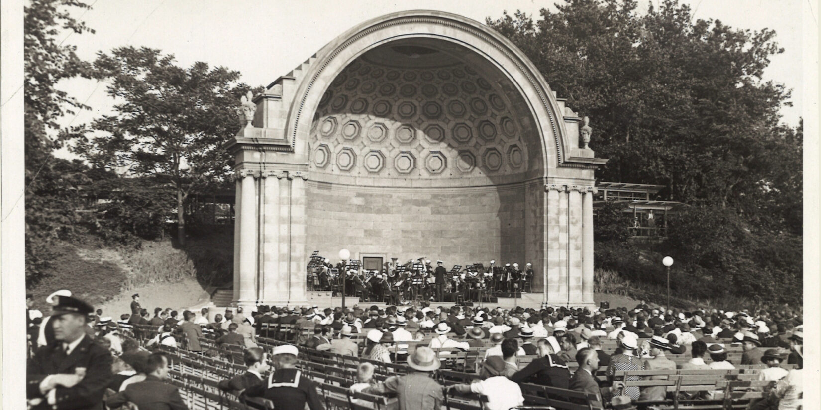 A black-and-white photo of the bandshell hosting a concert.