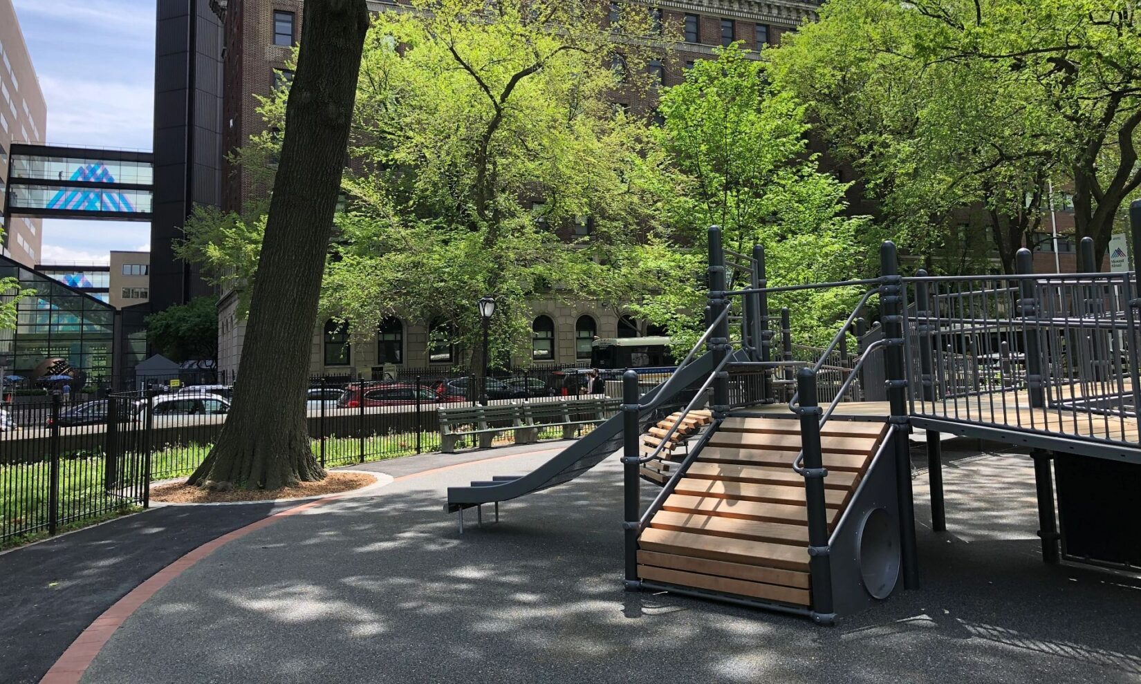 Play equipment is seen with buildings across the avenue as a backdrop