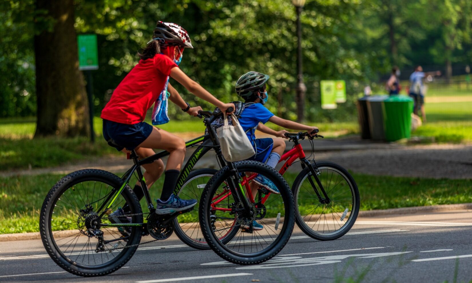 Two kids in helmets riding mountain bikes on a Park roadway