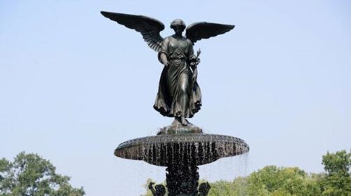 A closeup image of Angel of the Waters, the angel statue atop Bethesda Fountain, against a clear blue sky.