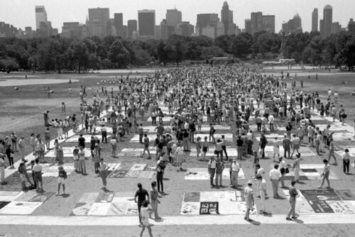 A black and white image of the AIDS quilt, spread out on the Great Lawn in Central Park, with the city skyline as a backdrop.