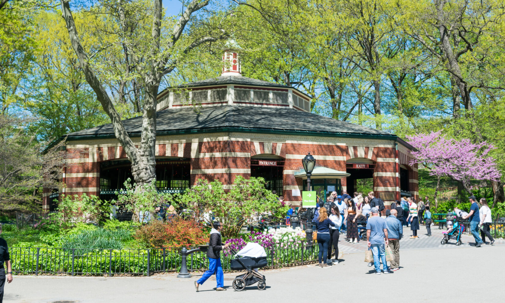 Families with toddlers and strollers crowd the plaza in front of the carousel on a clear spring day