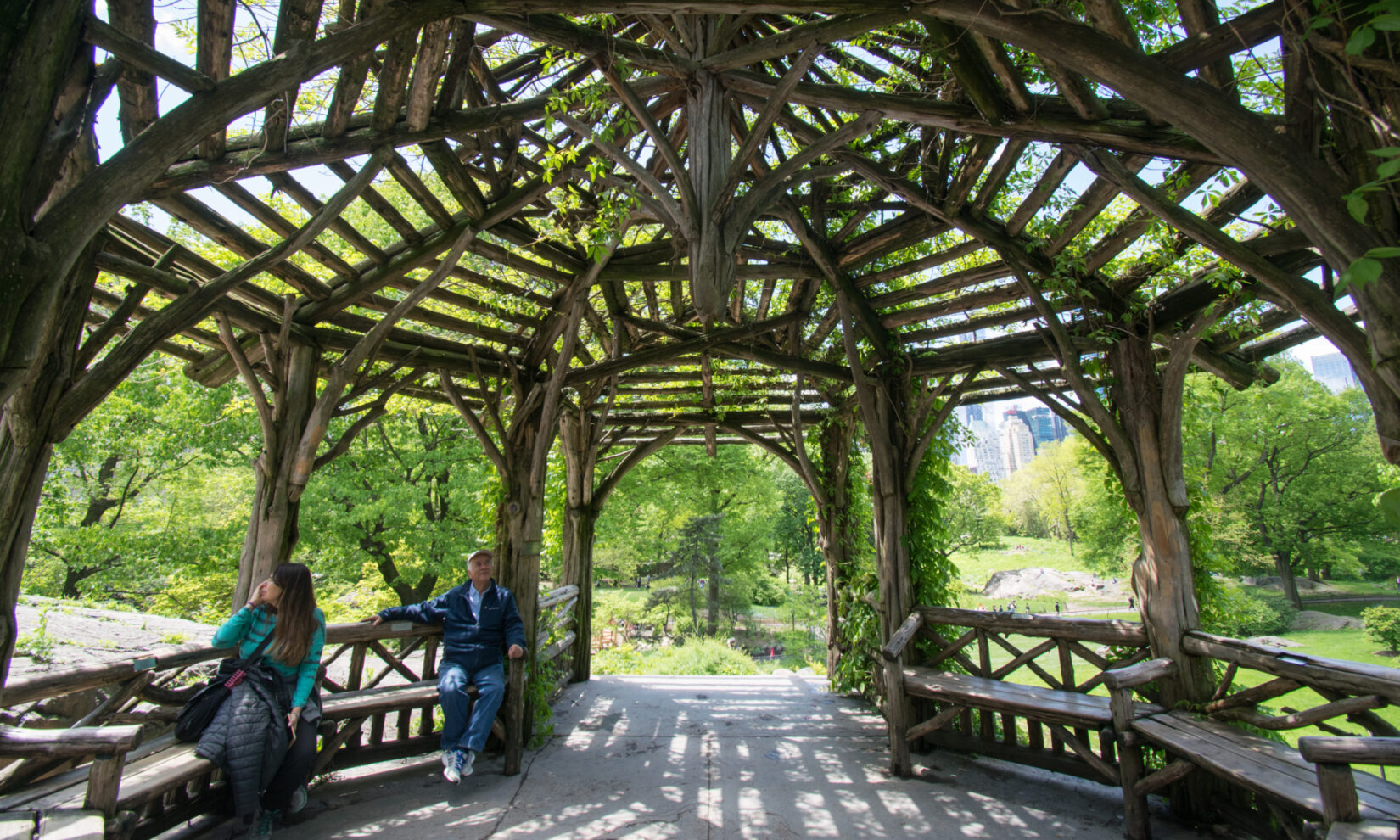 Two park-goers relax on benches under the timbers of the rustic summerhouse