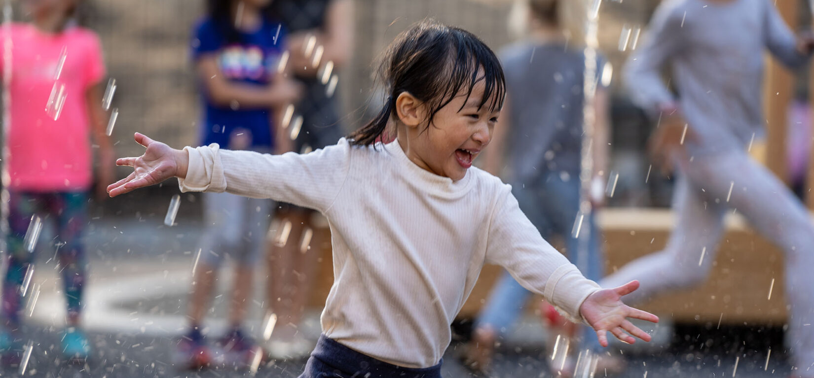 A young girl runs joyfully through the spray of a fountain