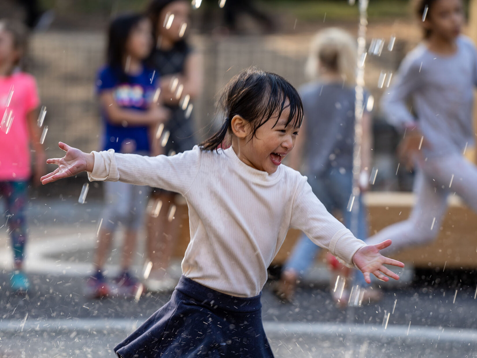 A young girl runs joyfully through the spray of a fountain