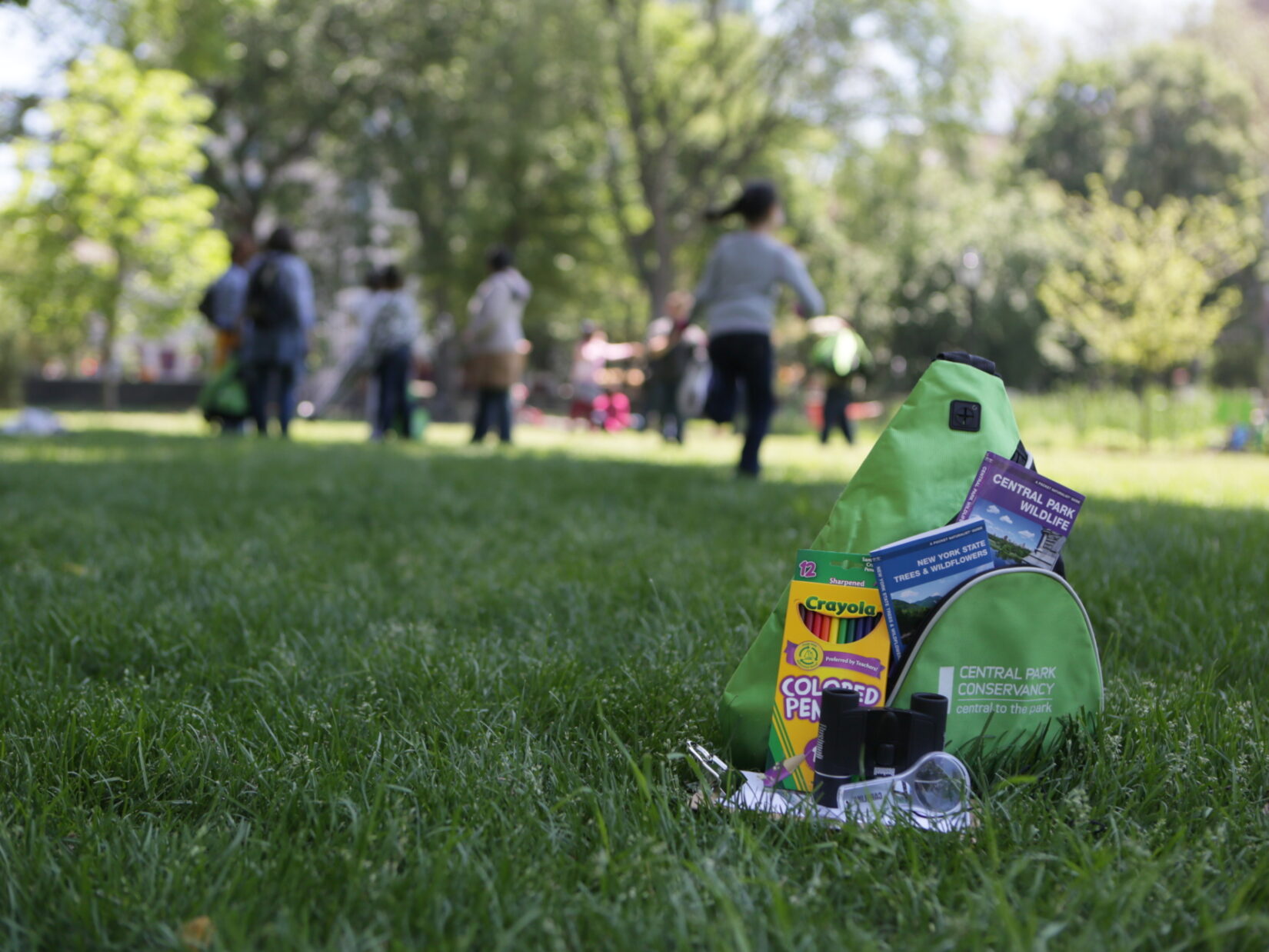 A Discovery Kit with crayons, binoculars, and other goodies, pictured on a lawn in summer