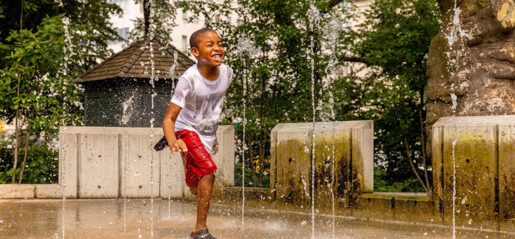 A young boy scrambles between water spouts in a Park playground.