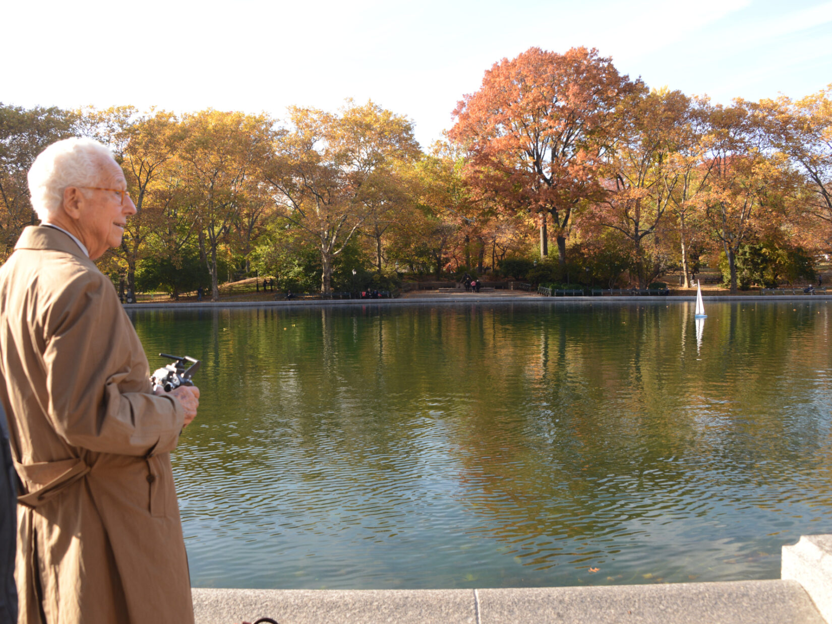 Ira Millstein standing in front of Conservatory Water, framed by fall foliage.