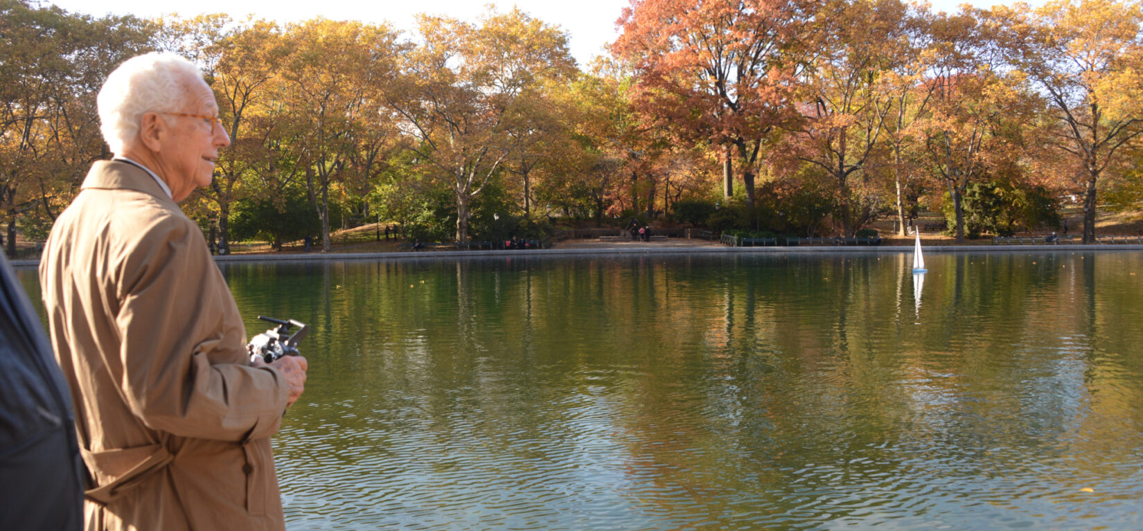 Ira Millstein standing in front of Conservatory Water, framed by fall foliage.