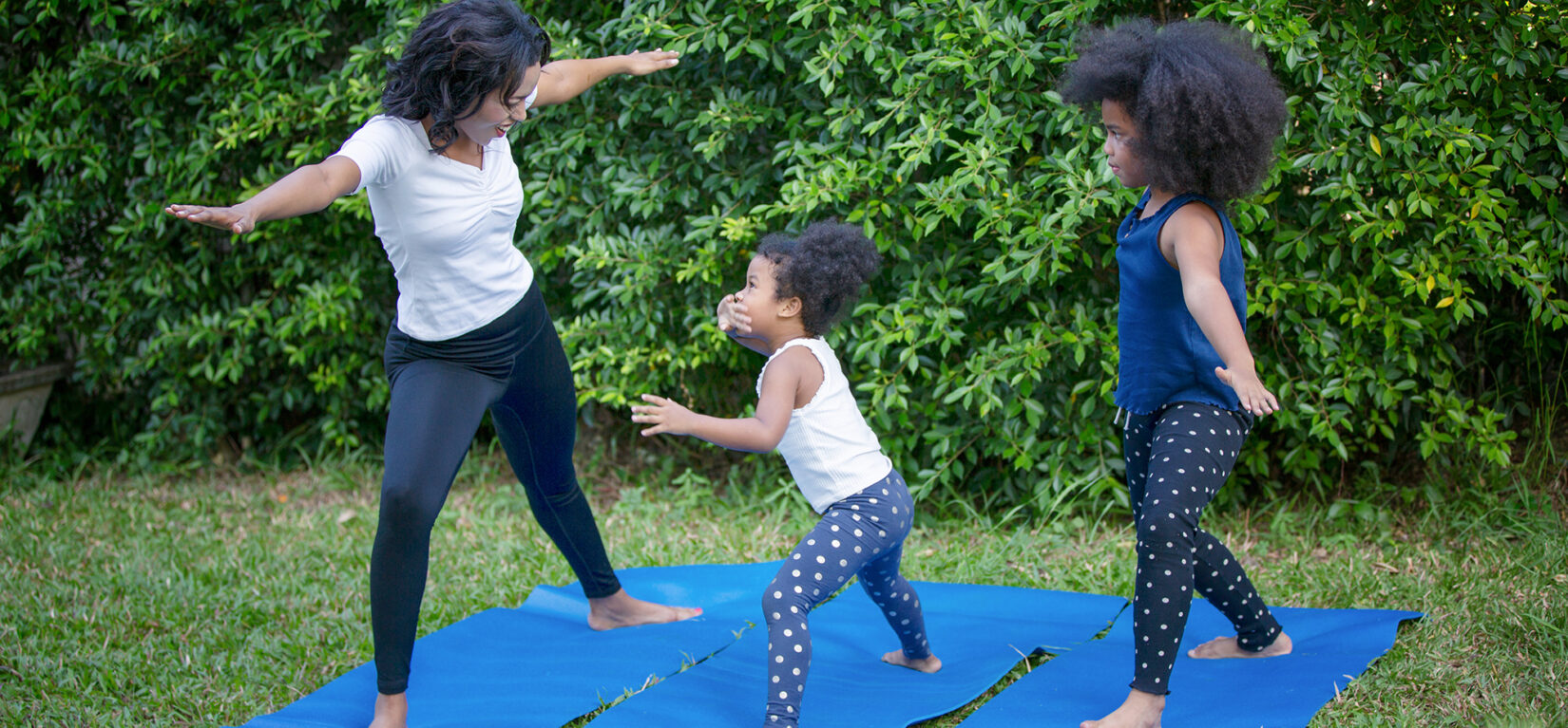 An adult and two young kids enjoying yoga in the Park.