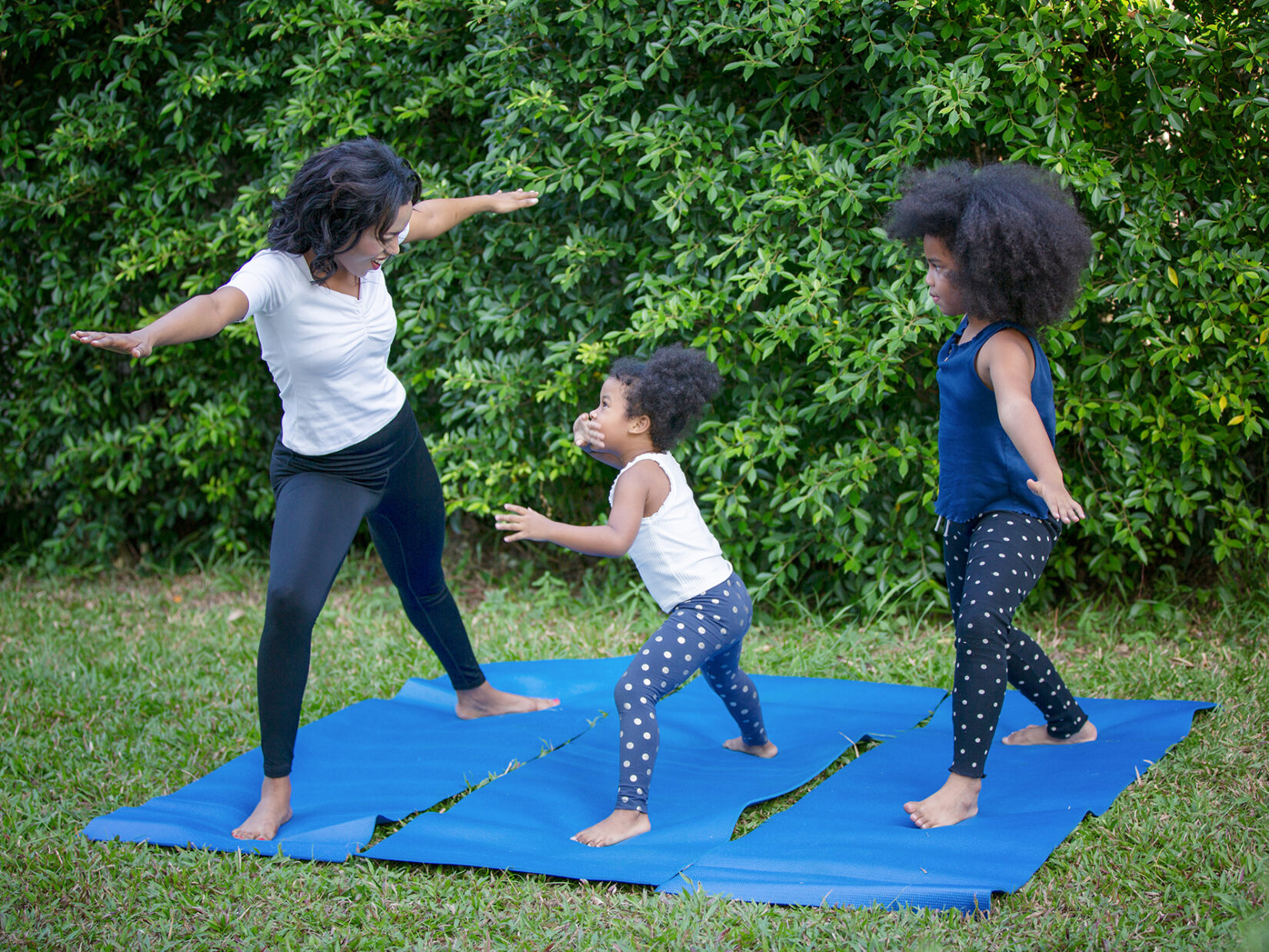 An adult and two young kids enjoying yoga in the Park.