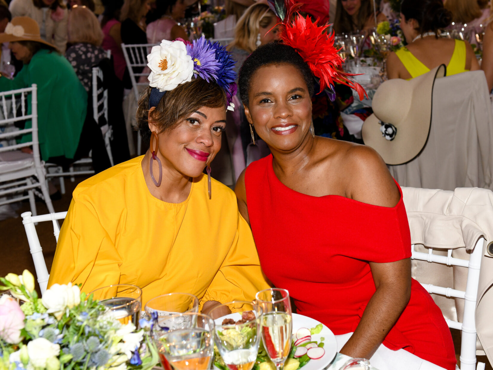 Two women sporting flowered hats enjoy the luncheon