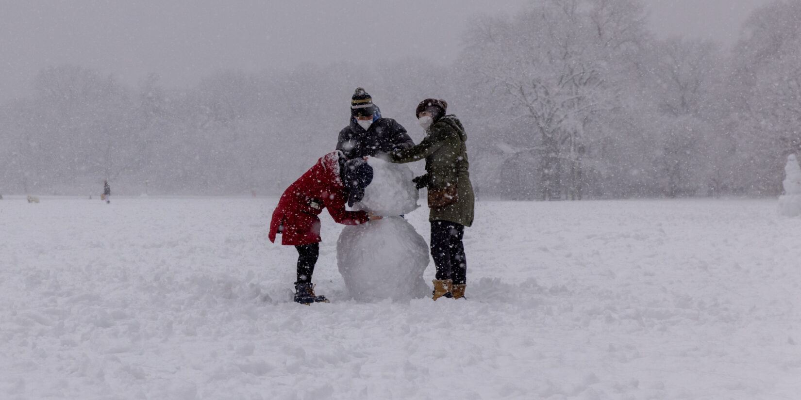 Three parkgoers building a snowman in the middle of a blizzard.