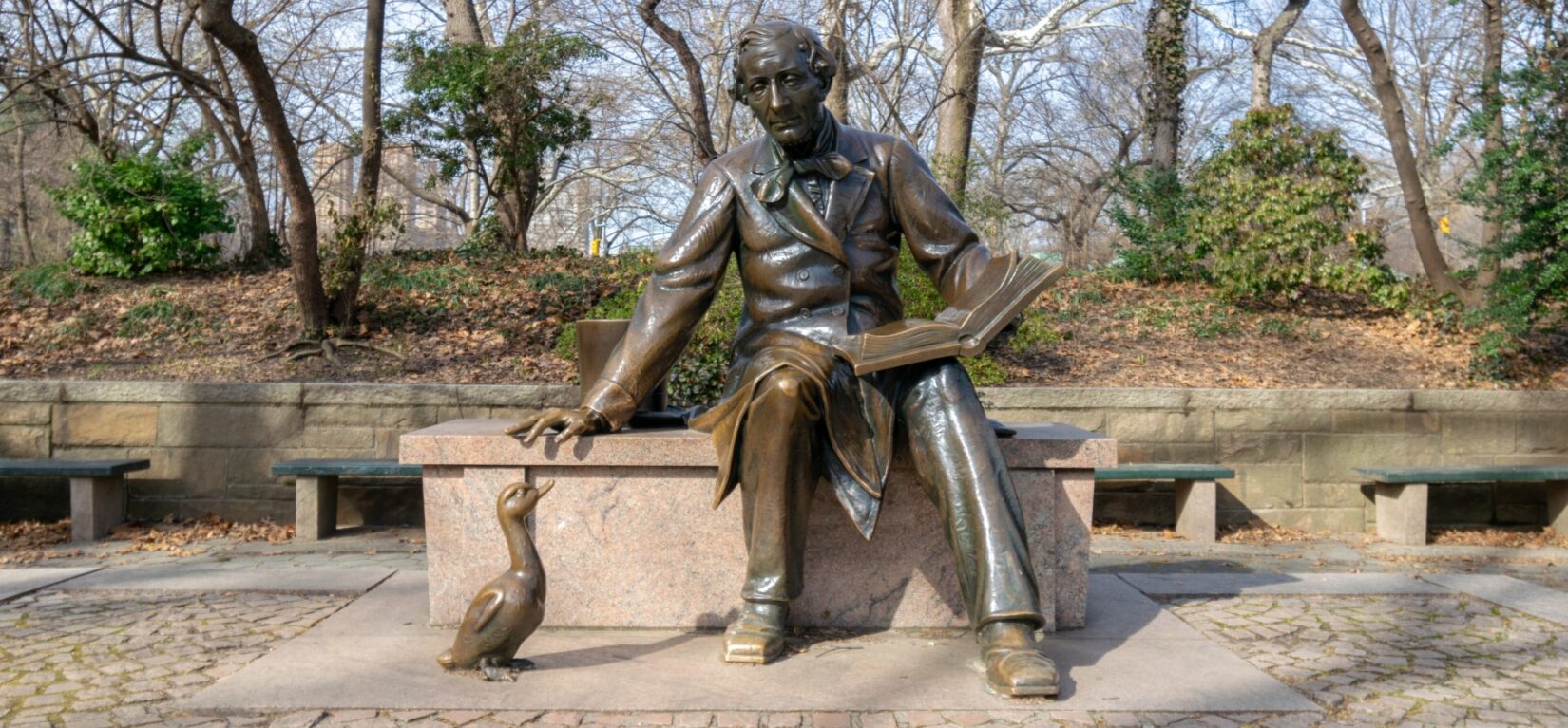 The statue shows the author with an open book on his lap and a duckling at his feet