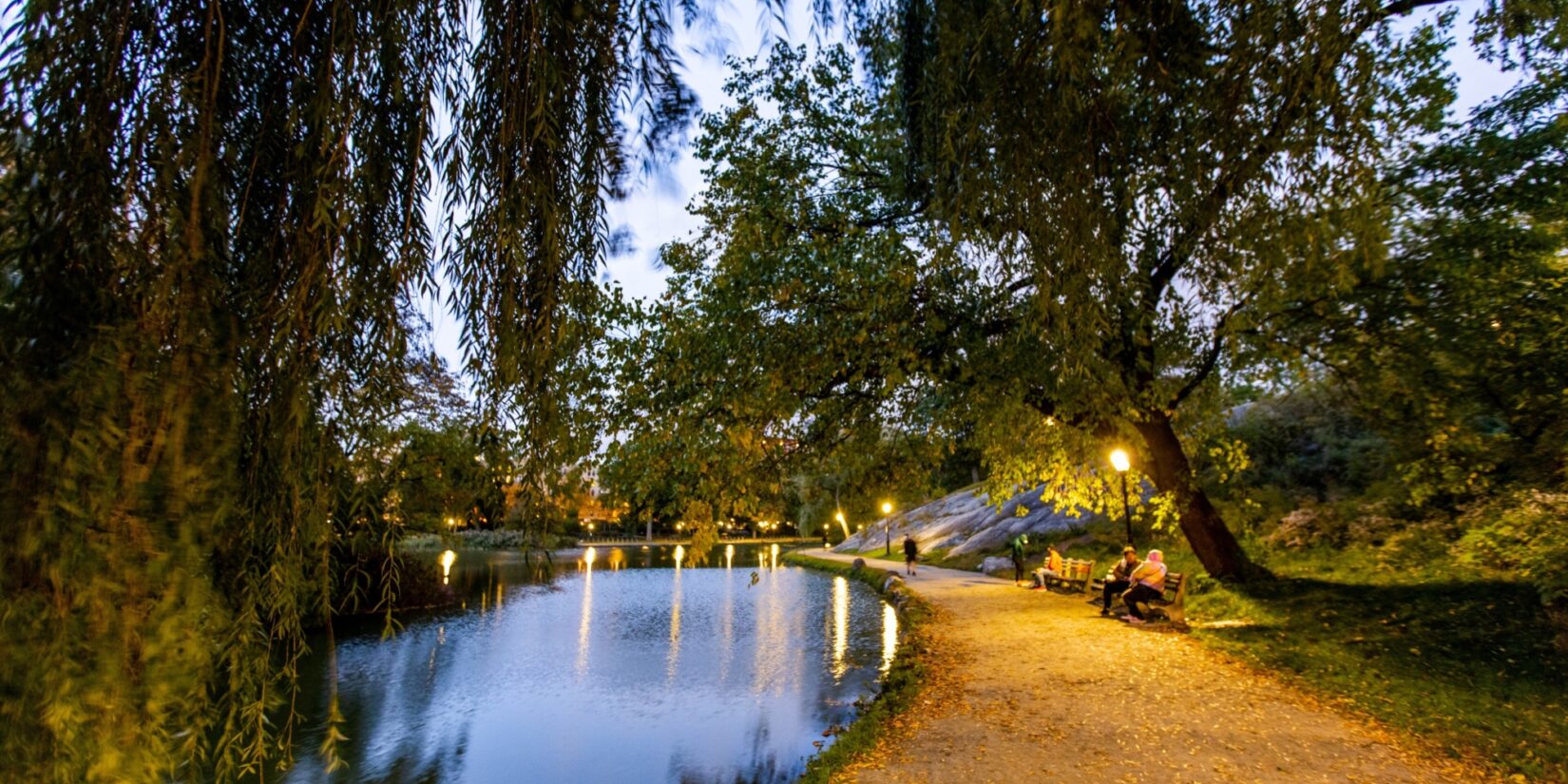 A couple sits on a bench on the winding banks of the Harlem Meer in twilight