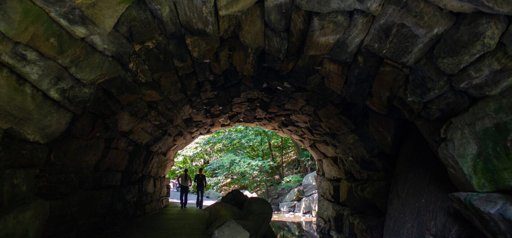 Two people strolling the narrow footpath beneath the Huddlestone Arch