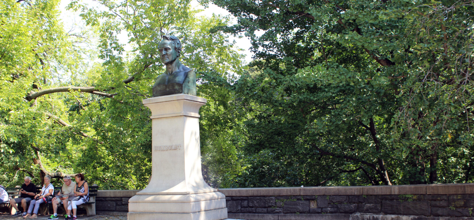 Visitors sit on a park bench with a view of the Humboldt statue