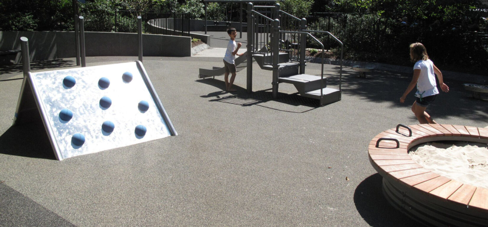 Children run between the play equipment on a bright, sunny day.