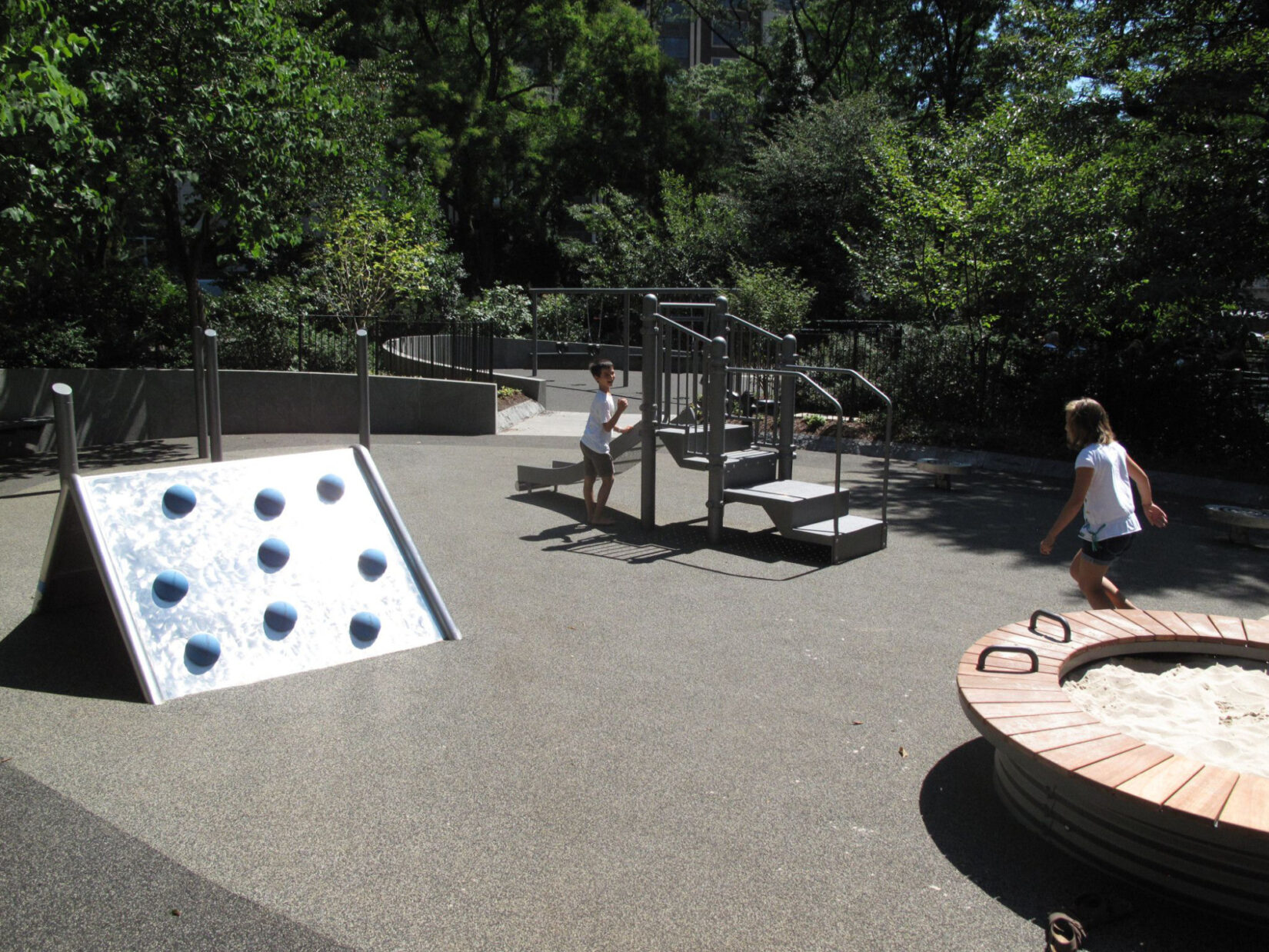 Children run between the play equipment on a bright, sunny day.