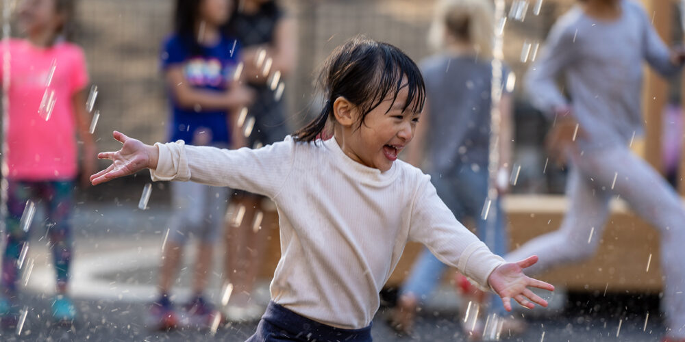 A young girl enjoys running through the spray of a water feature