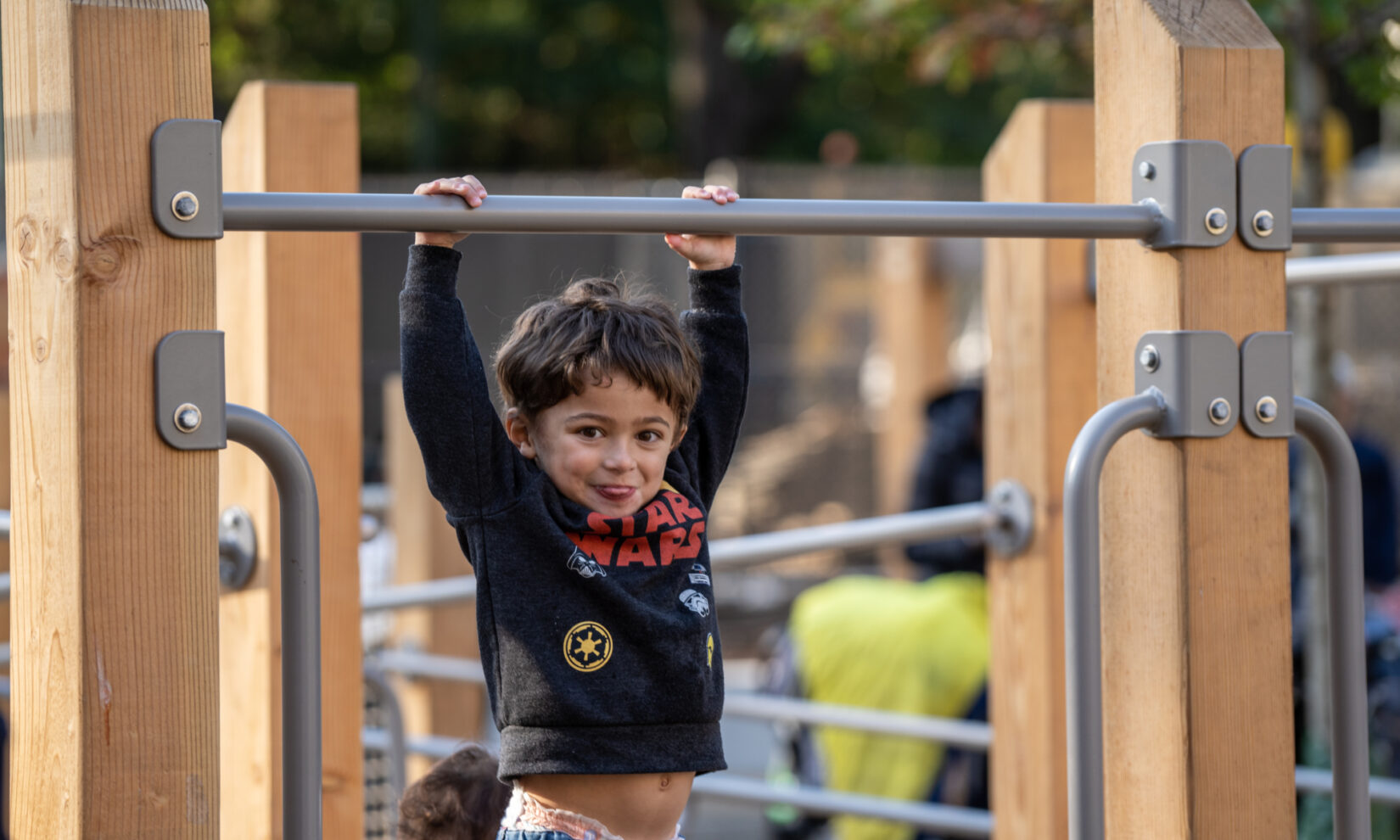 A very young child hangs from a bar on the climbing equipment of the playspace.