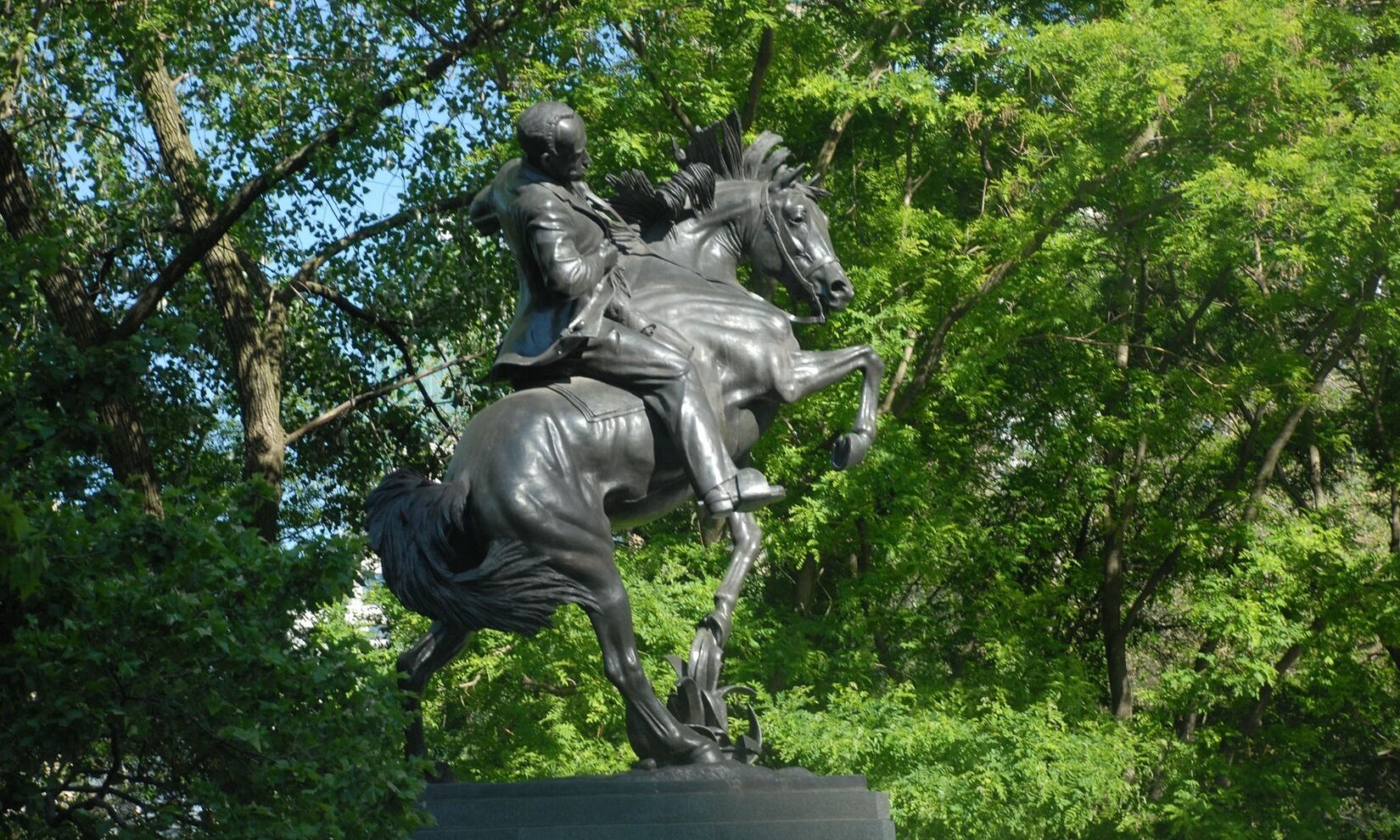 The statue is seen against dense summer foliage