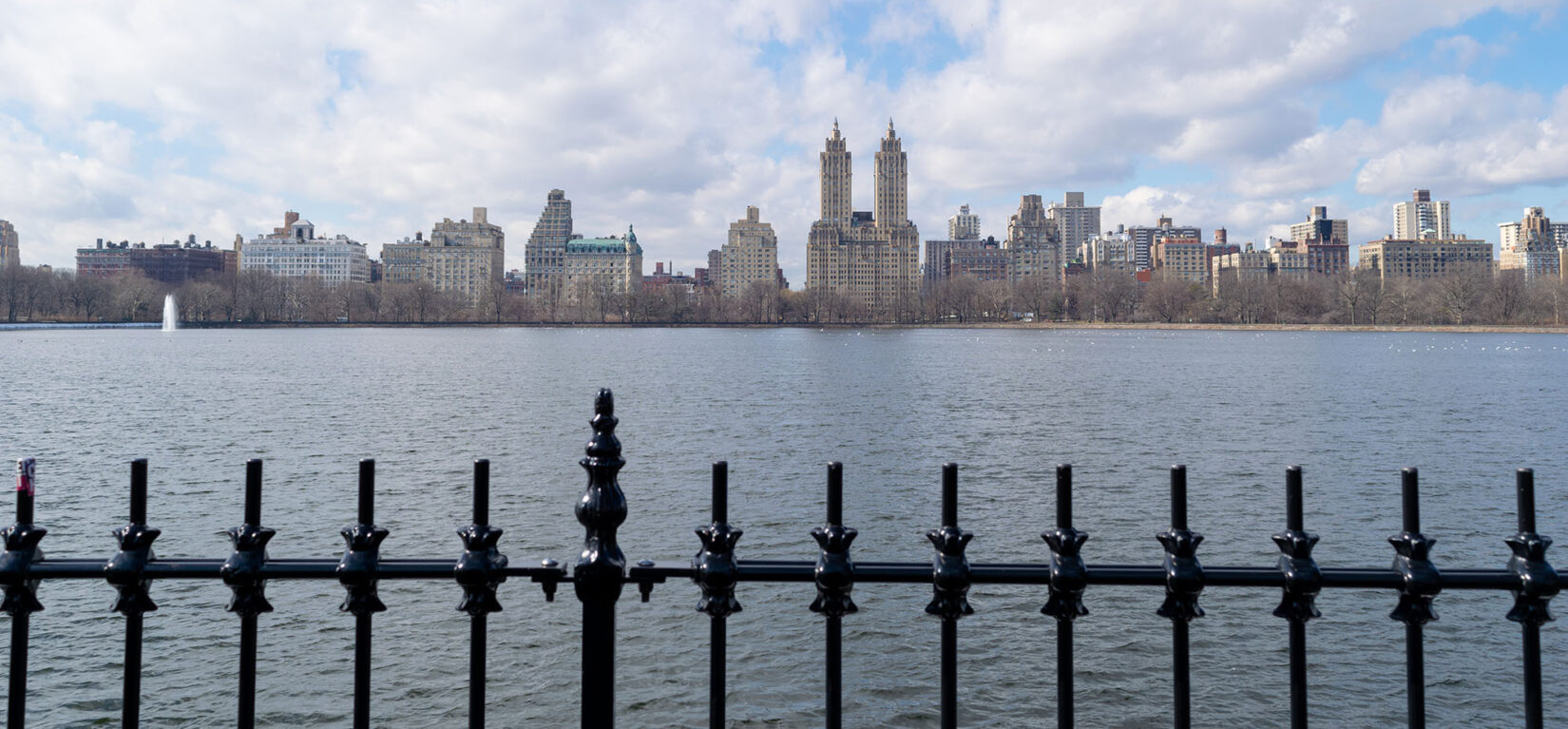 Looking across the Reservoir on a cloudy day with the ironwork of the fence in the foreground