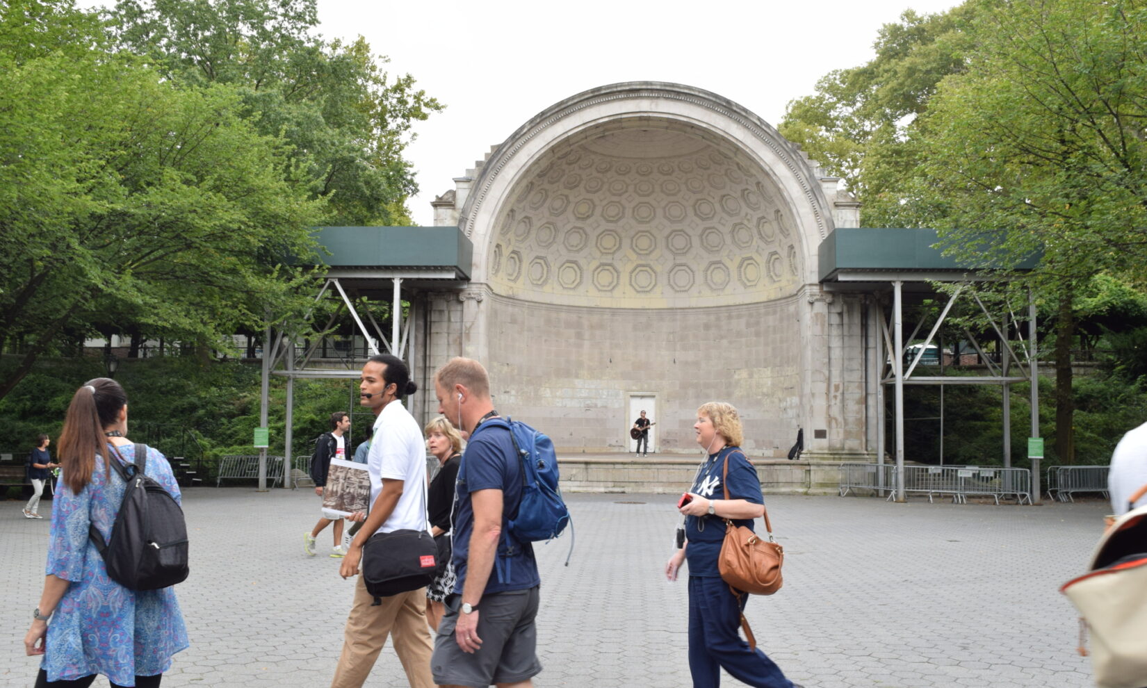 Park-goers pass a lone guitarist testing the acoustics of the bandshell.