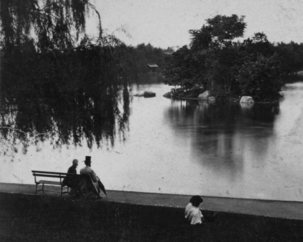 Antique photo showing a couple on a bench by the Lake, with the gentleman wearing a top  hat