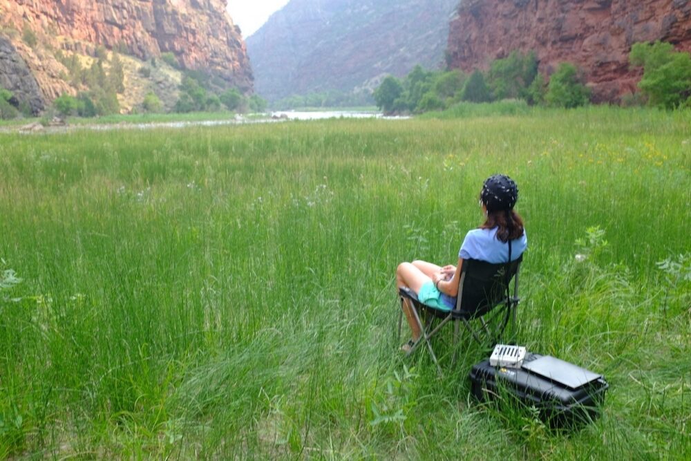 A woman wearing brain-scanning apparatus sits in a mountain glen