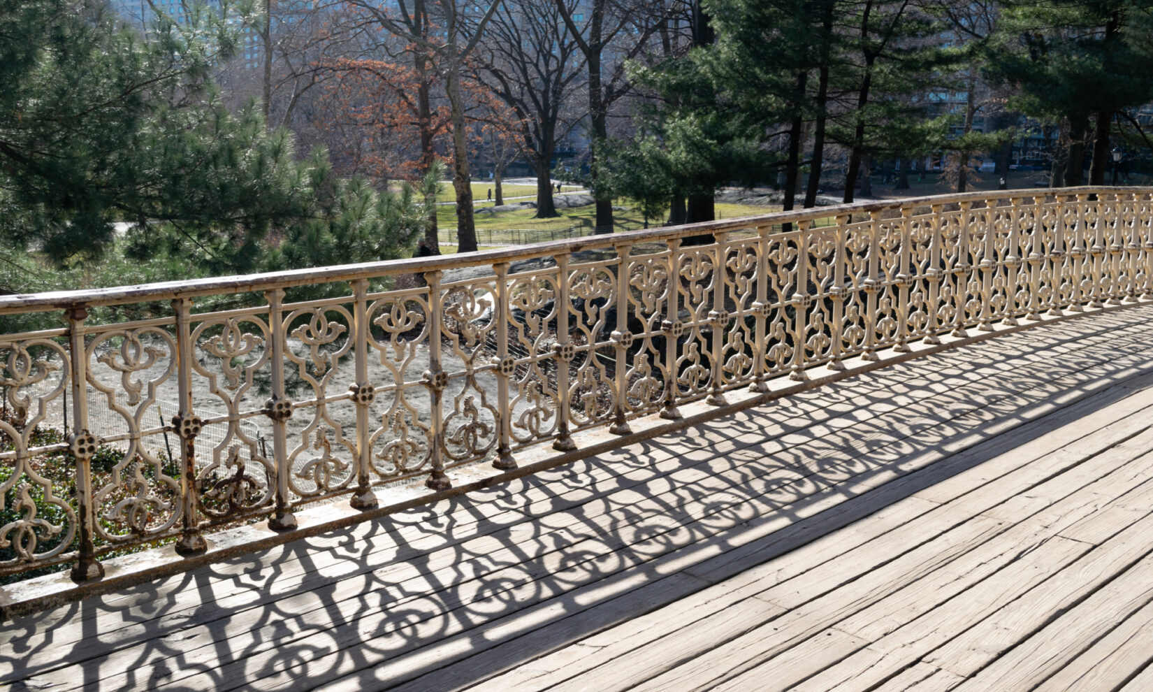 The intricate ironwork of the arch casts interesting shadows on  wooden planking.