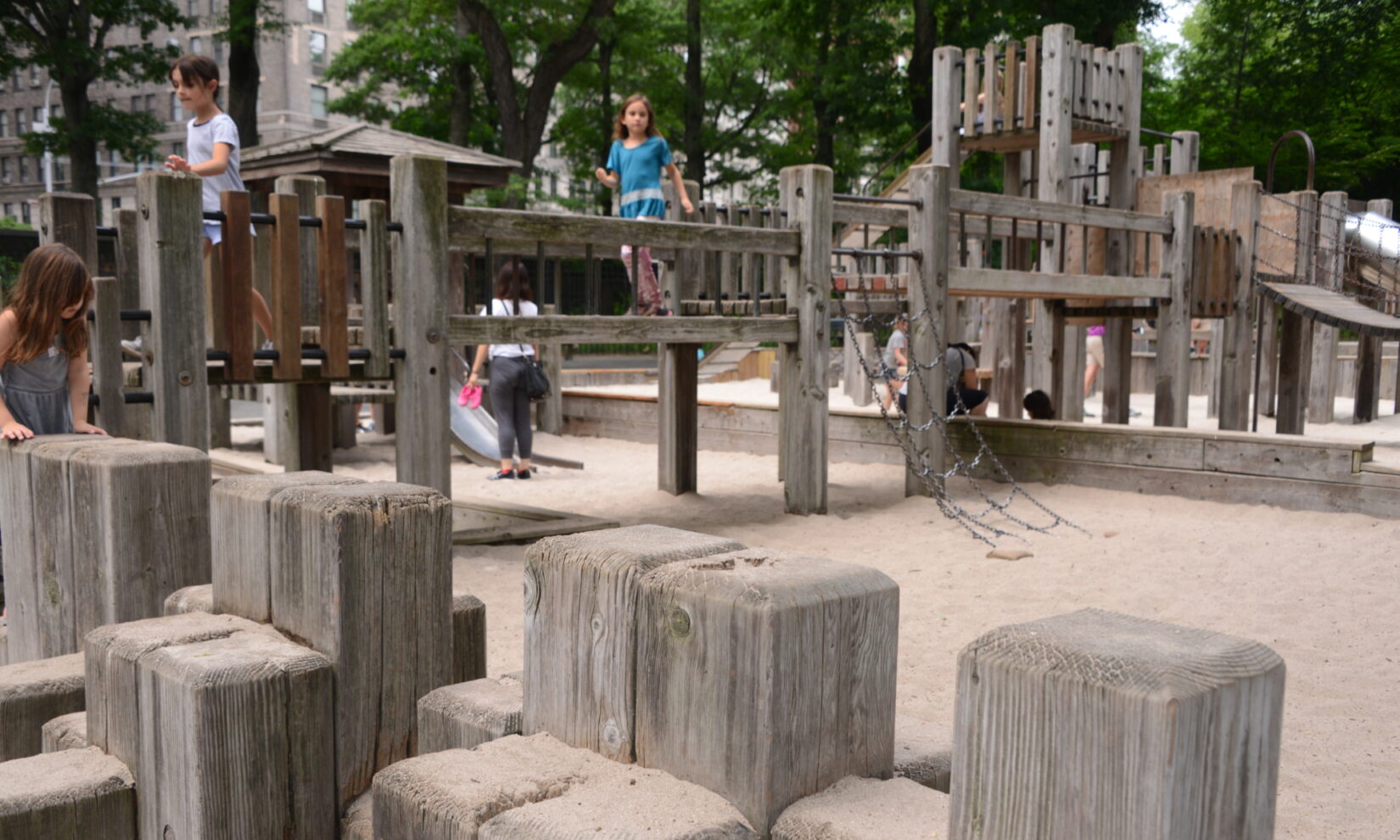 A girl crosses a wooden bridge spanning a sand pit in the playground.