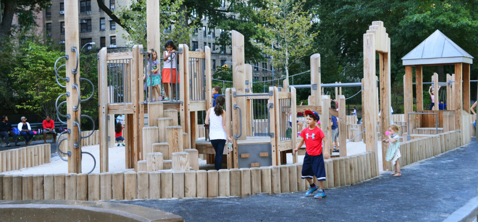 Wooden play structures surround sandy ground, surrounded by a path.