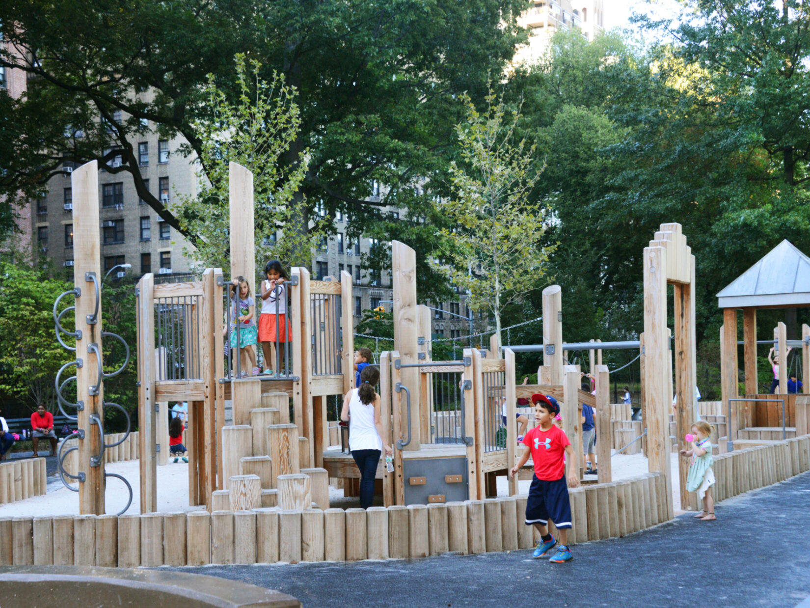 Wooden play structures surround sandy ground, surrounded by a path.