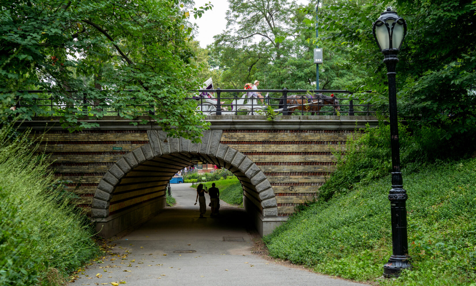 Strollers beneath the arch seem unaware of the horse and carriage on the drive above it.