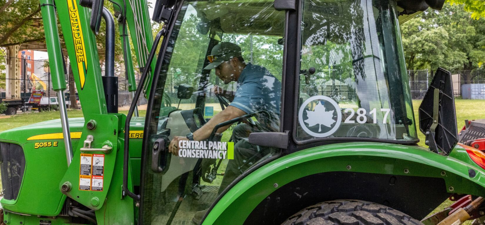 A man operates a large green machine in a park.