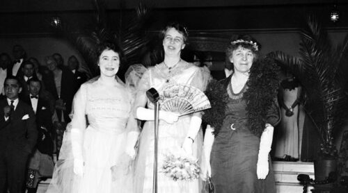 Eleanor Roosevelt is flanked by Rumsey and Greenway in front of a microphone