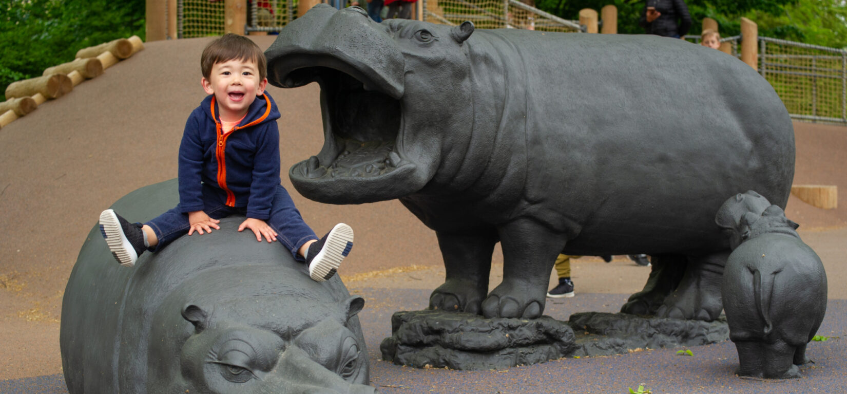 A small child sits atop one of the sculptures of a hippo in the playground.