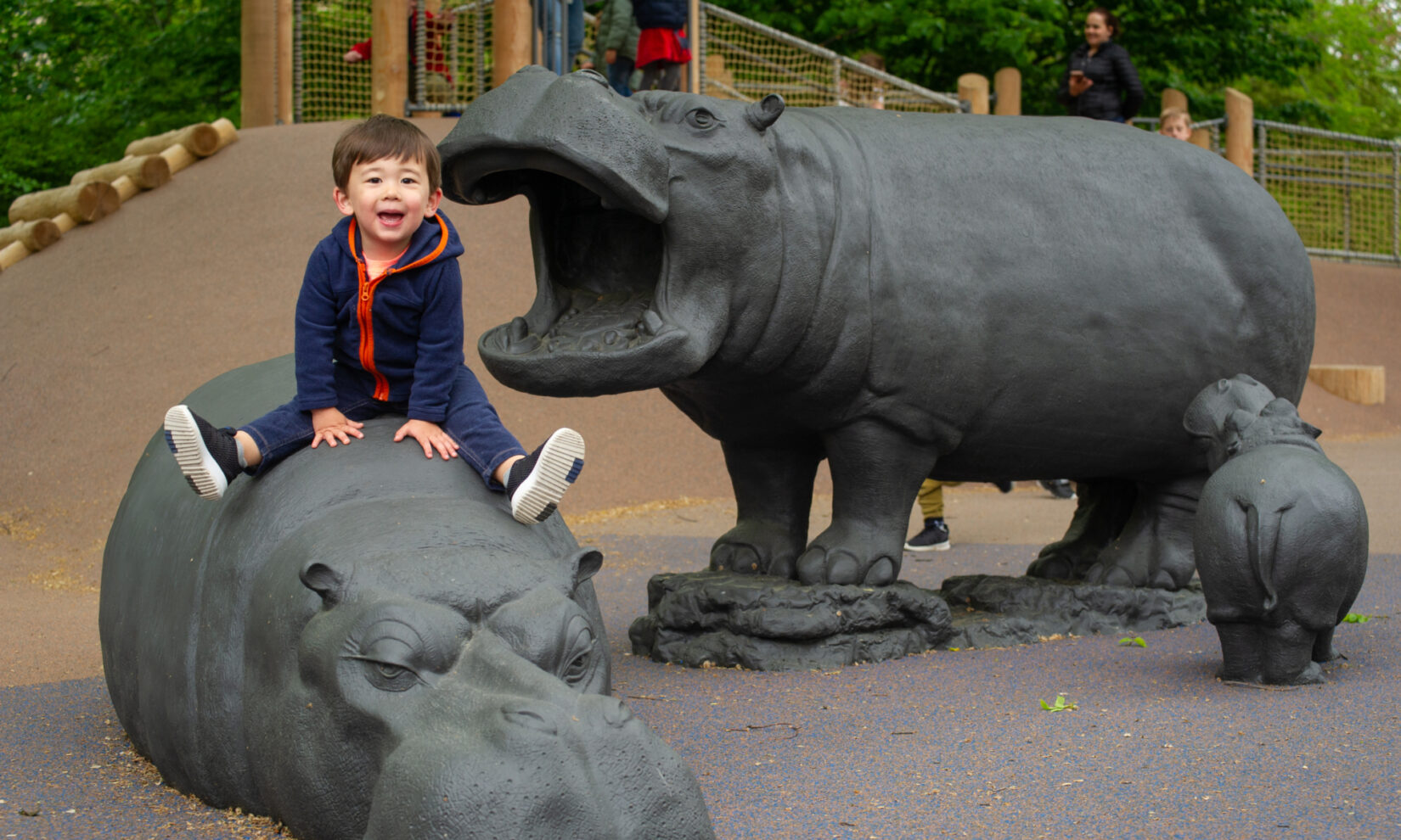 A small child sits atop one of the sculptures of a hippo in the playground.