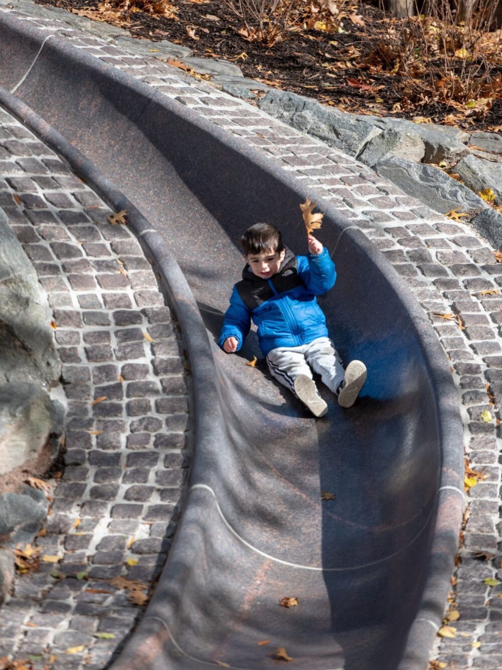 A young boy slips down the long, curving sliding pond