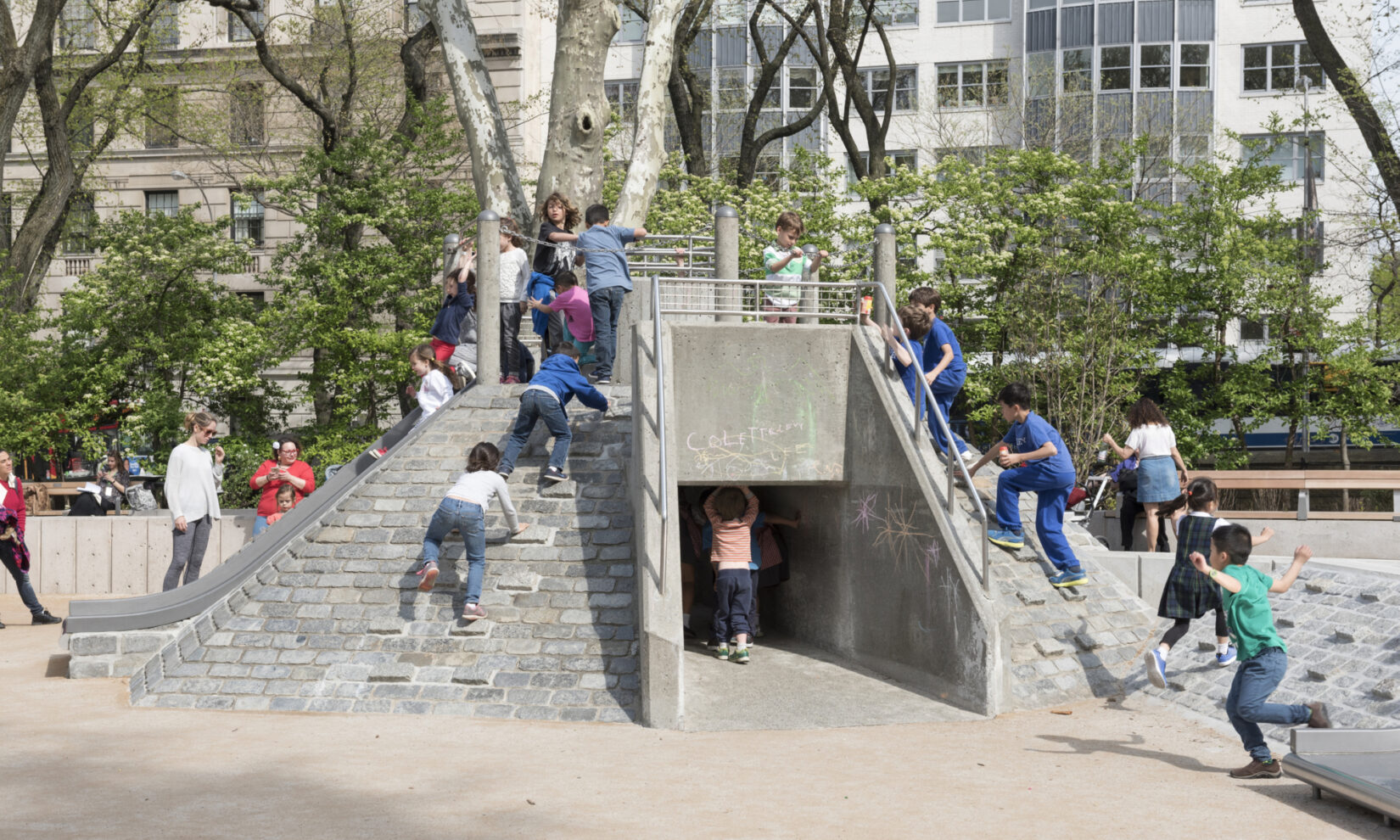 Kids clamber over, and walk under, the stone climbing apparatus in the playground.