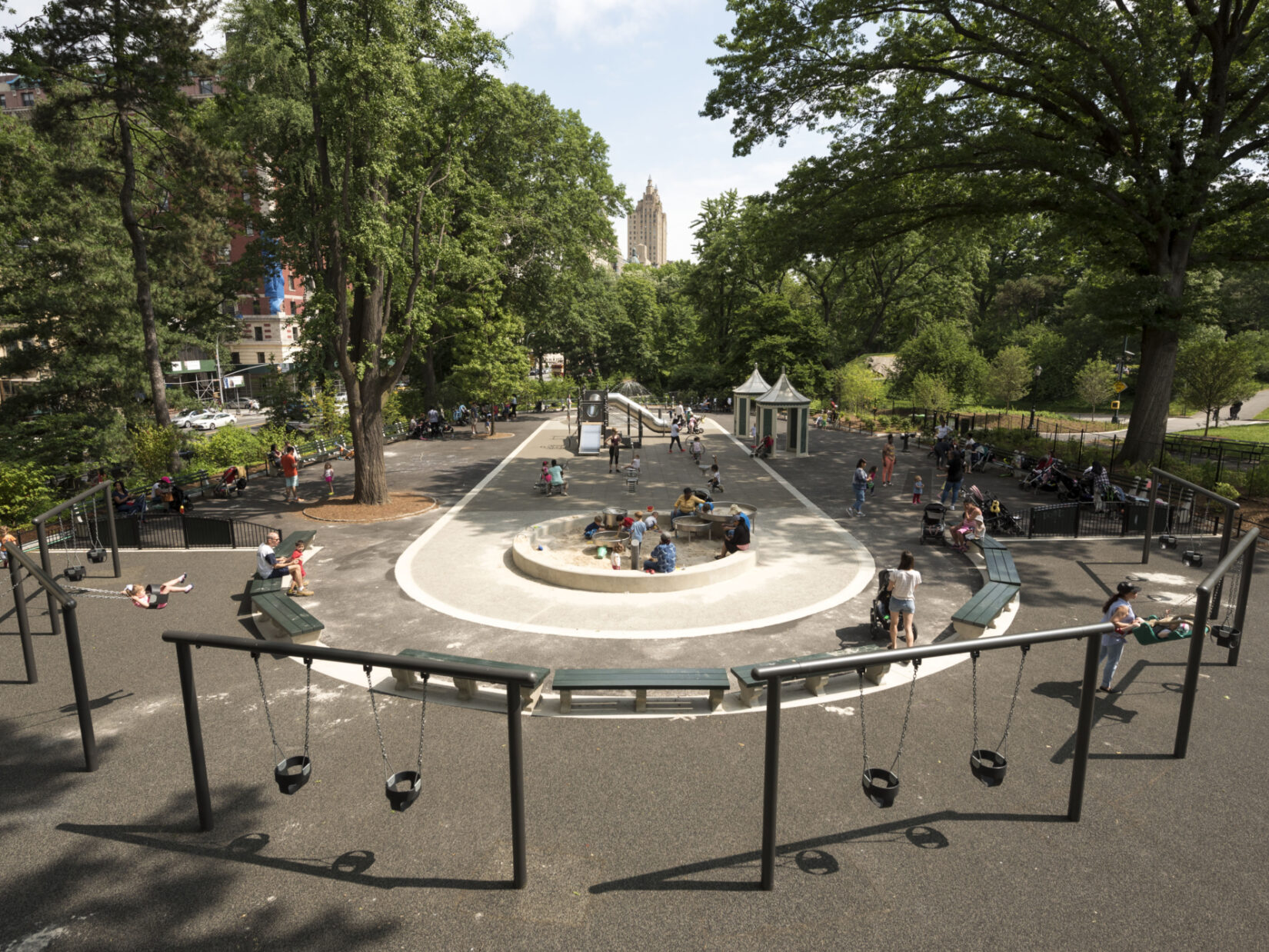 A wide-angle view down the length of the playground, shot from above and behind a row of infant swing sets.