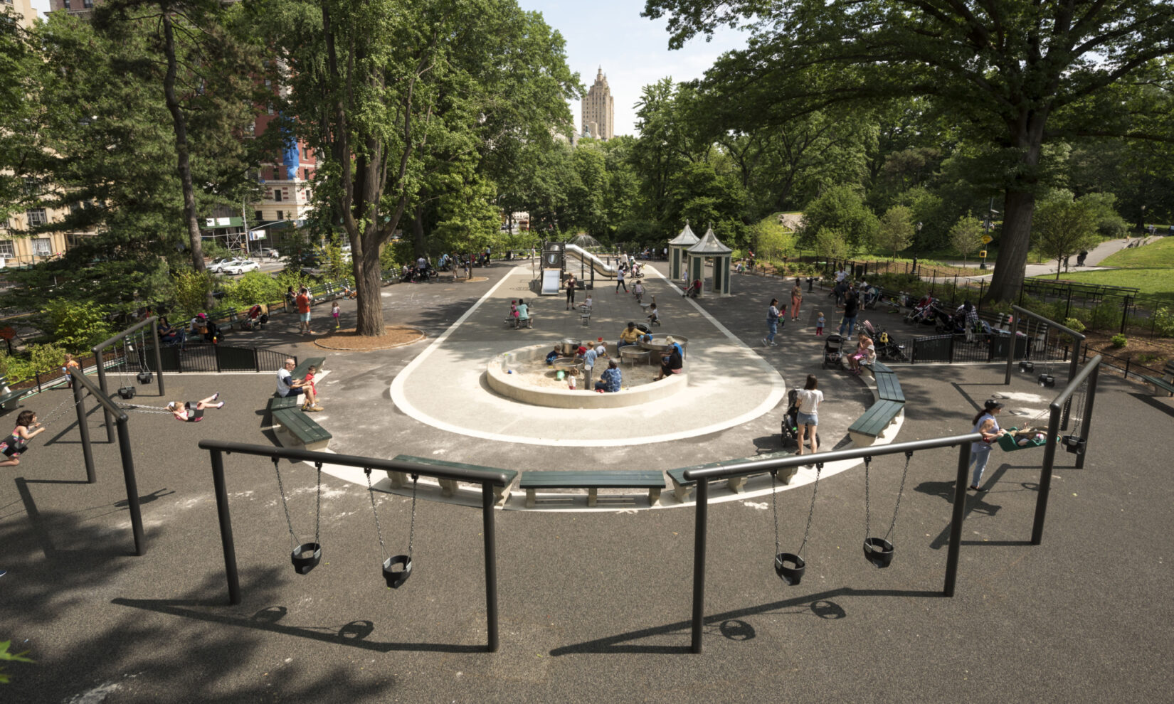 A wide-angle view down the length of the playground, shot from above and behind a row of infant swing sets.